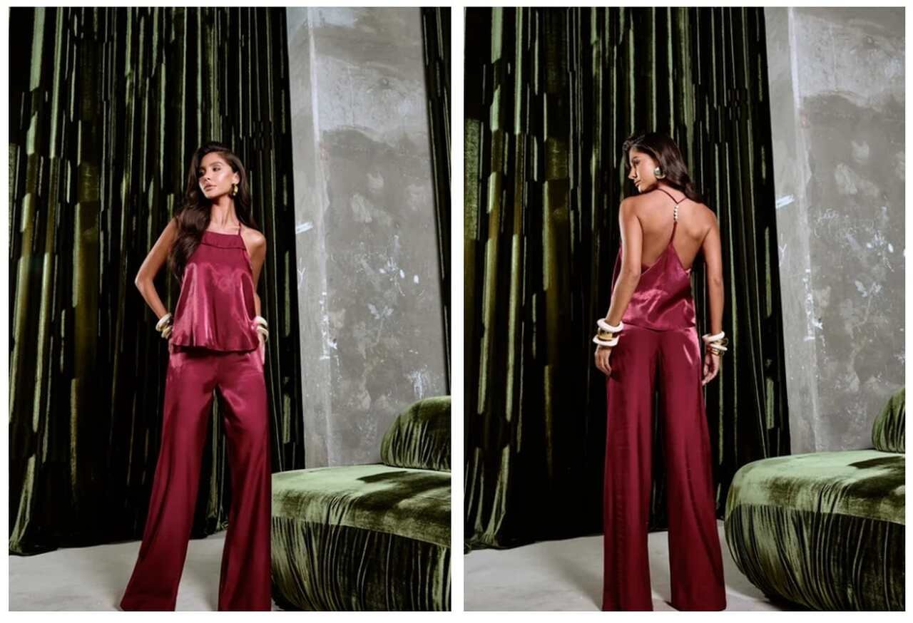 Mulher exibe conjunto de cetim com top frente &uacute;nica e cal&ccedil;a ampla, ideal como inspira&ccedil;&atilde;o de looks para o Natal. Fundo elegante com cortinas e banco de