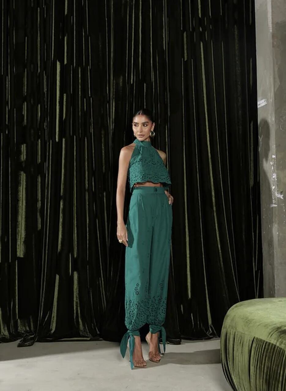 Pessoa em look verde vibrante com recortes modernos, em frente a cortina de veludo. Inspira&ccedil;&atilde;o ousada nas co