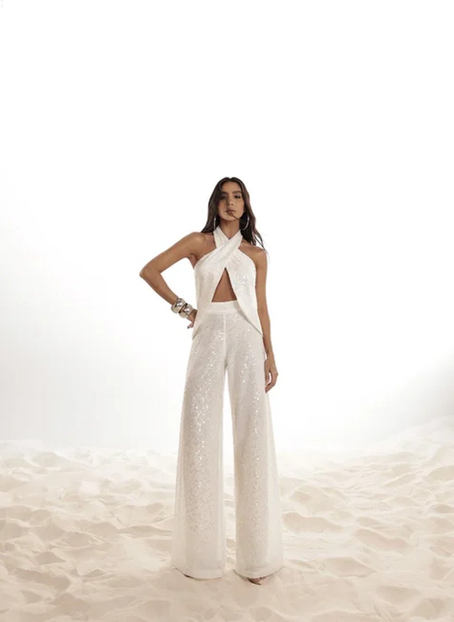 Pessoa em look branco elegante sobre areia, vestindo top com recortes e cal&ccedil;a brilhante. Inspira&ccedil;&atilde;o moderna nas c