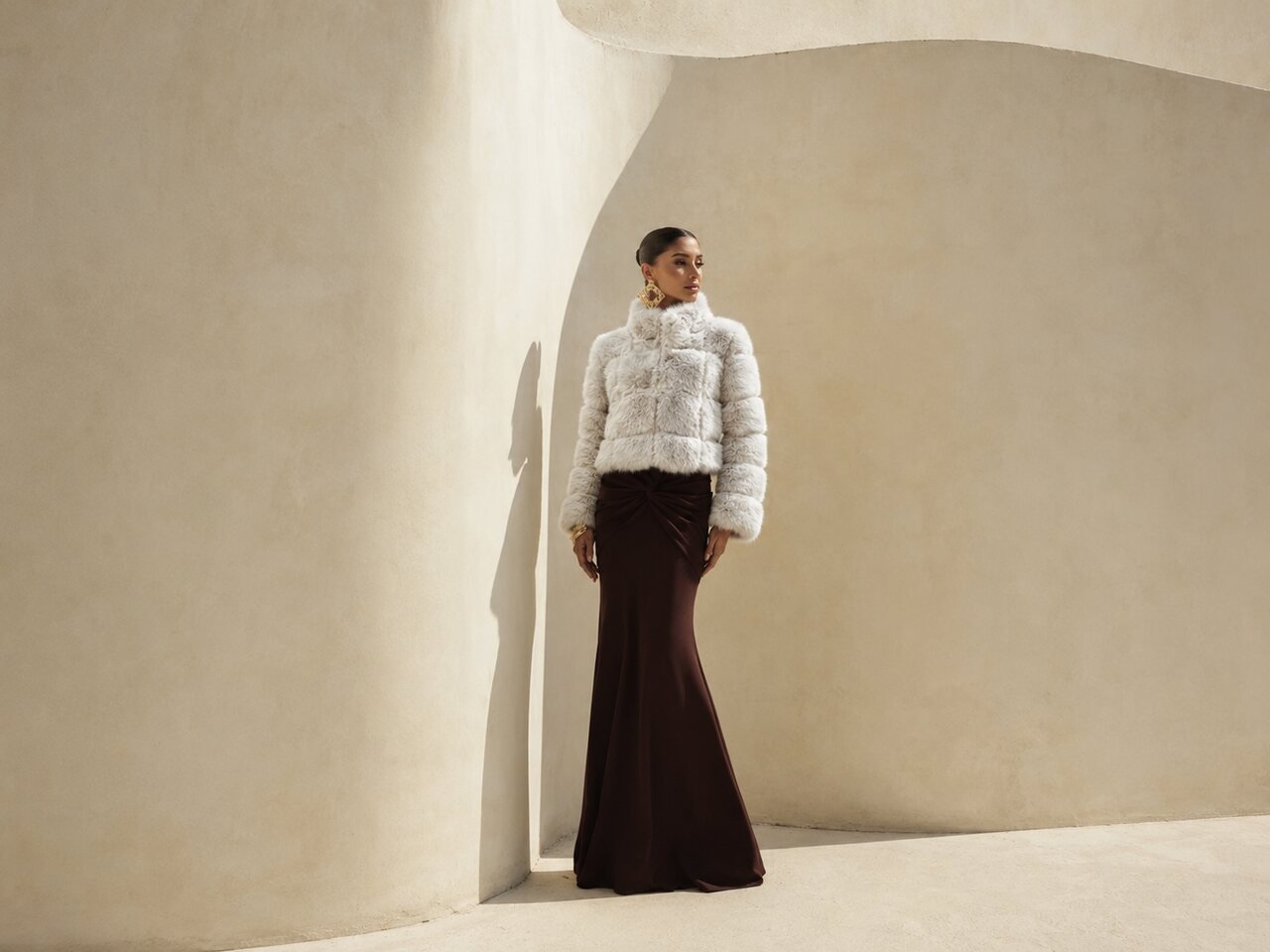 Mulher em casaco para usar com vestido de festa branco, jaqueta de pele, vestido longo marrom em arquitetura minimalista bege moderna.