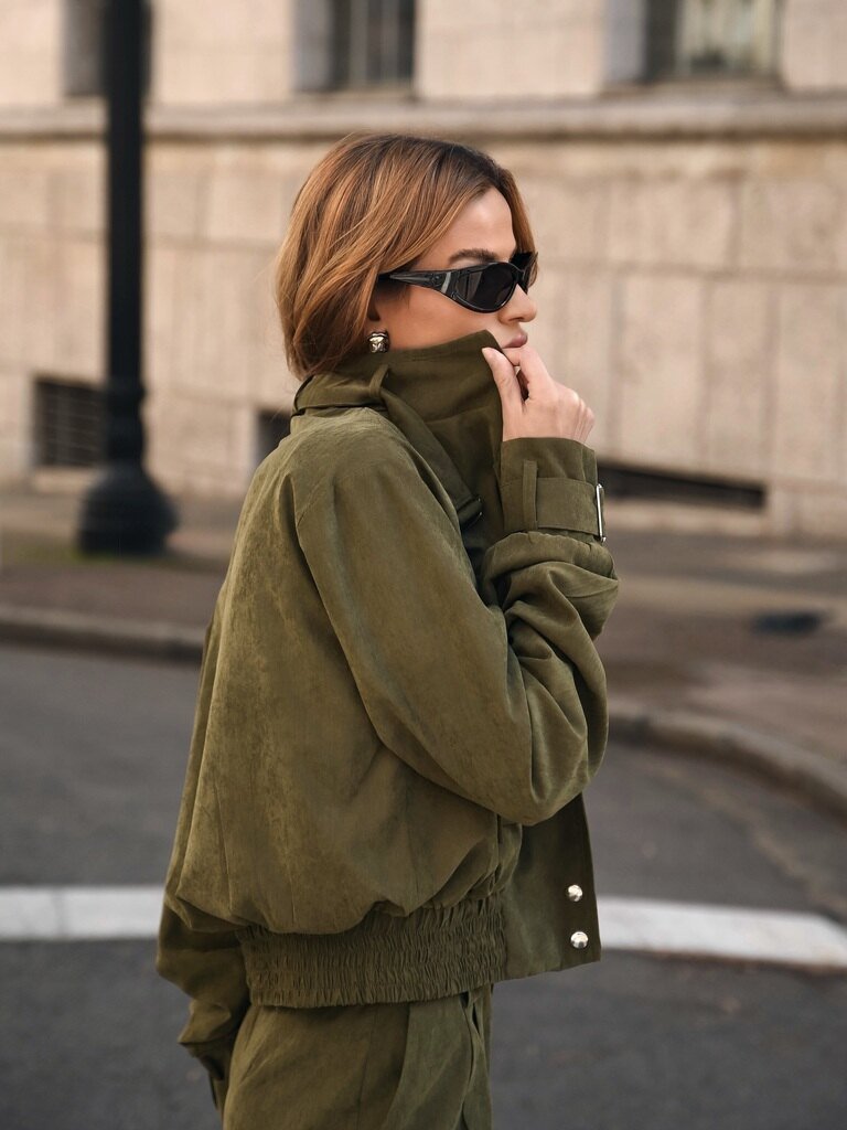 Pessoa em conjunto verde oliva com jaqueta de gola alta, óculos escuros e looks para inverno europeu sofisticados.